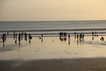 crowded beach. people on white sand beach against background of blue sea and orange sky at sunset on kuta beach bali