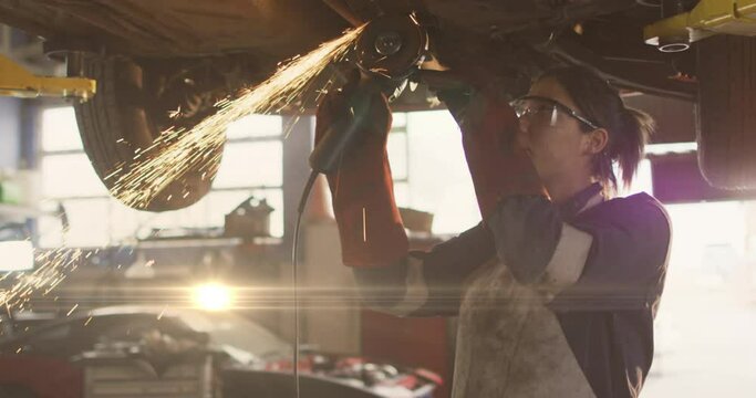 Animation of glowing light over caucasian female car mechanic working in workshop