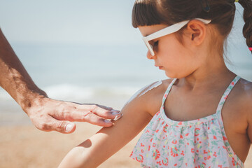 father smears her daughter with sunscreen on the beach in summer, the concept of safe tanning