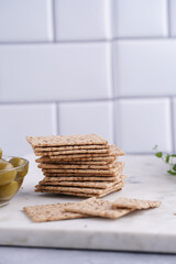 Fototapeta na wymiar Healthy crunchy crisp crackers with sesame seeds and green olives on marble board