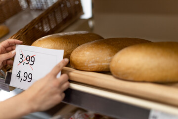 Woman shop assistant changing prices of bread in supermarket, the concept of increasing inflation