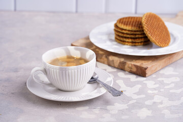 Stroopwafel - traditional dutch sirup waffles with caramel filling - stacked on top of each other on a wooden board, white kitchen and a cup of coffee in white porcelain cup