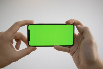 Holding an iPhone in hand. Green Screen on the phone. Mock-up of an iPhone. Apple product in hand. Vertical tilt of the phone.