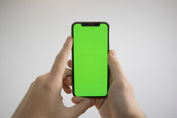 Holding an iPhone in hand. Green Screen on the phone. Mock-up of an iPhone. Apple product in hand. Vertical tilt of the phone.
