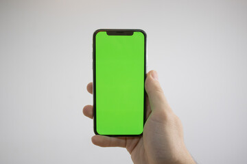 Holding an iPhone in hand. Green Screen on the phone. Mock-up of an iPhone. Apple product in hand. Vertical tilt of the phone.