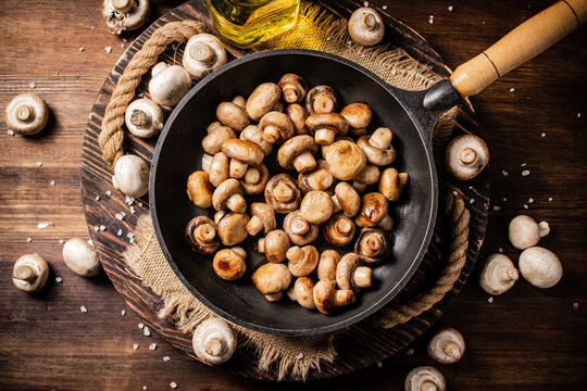 Frying pan with fried mushrooms on a wooden tray. On a wooden background. High quality photo