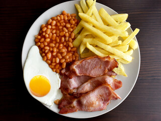 Back bacon, egg, chips and beans on a plate.