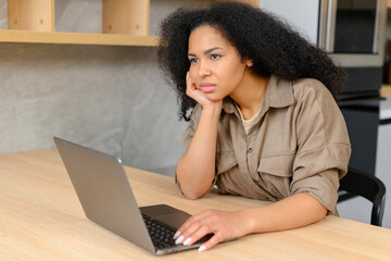 Sad multiracial woman looking annoyed and stressed, sitting at the desk, using a laptop, thinking, feeling tired and bored with depression problems