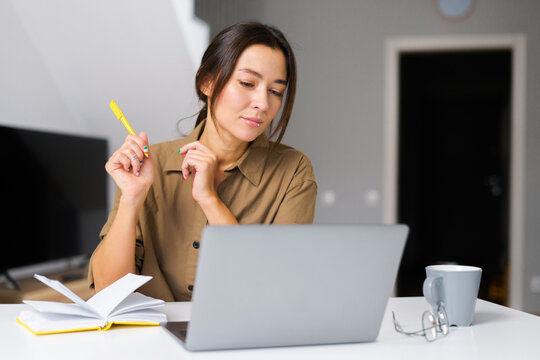 Smiling asian businesswoman taking notes sitting at the desk in modern office space. Young multiracial female student overwrites from the laptop screen into notebook