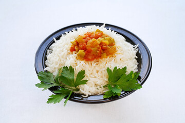 White basmati rice with stewed zucchini, tomato and other vegetables on top and served on a black ceramic plate. High angle. Light background 
