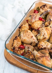 Blurred image of baked chicken legs with vegetables in a glass bowl.