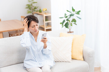 ソファーに座るミドル女性（スマホ・メール・インターネット）