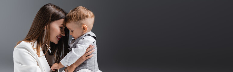 happy young woman smiling near little son on grey with copy space, banner.