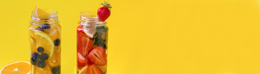 Banner of summer drink. Detox or infused water with fruit and berry in the bottle on the yellow background. Copy space.