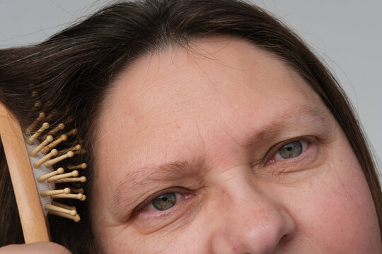 Close-up Of Mature Adult Woman Brushing Her Hair, Combing Dirty Greasy Hair With A Wooden Massage Brush. Woman Serious Hair Loss Problem For Health Care Shampoo, Beauty Product Concept, Haircut Care