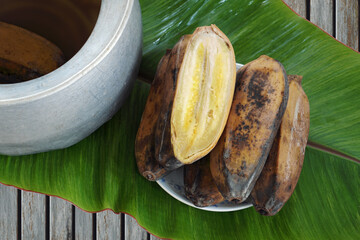 Boiled Saba bananas are placed in a plate and green banana leaves are laid on the table. Boiled bananas are popular for breakfast and hot beverages in Asian countries.