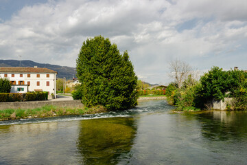 Fototapeta na wymiar Meschio river flowing among the houses under the cloudy sky.