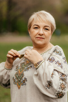 pretty senior woman in traditional ukrainian embroidered shirt on park background