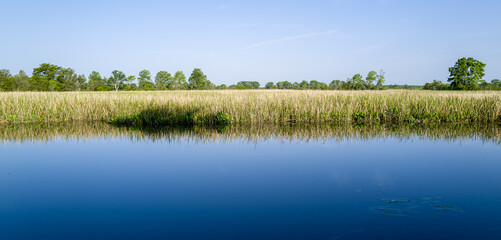 Fototapeta na wymiar Calm river water reflections under blue sky