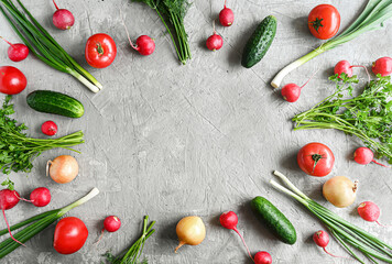 Whole fresh healthy vegetables: tomatoes, cucumbers, radishes, onions and herbs on a light gray table. Top view from the copy space.