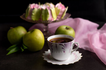 Blurred image of a cup with coffee, apples and dessert on glassware on a black background.