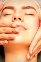 Beautiful young caucasian woman with closed eyes receiving a facial massage in a beauty salon