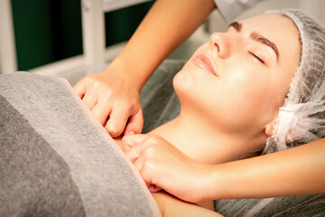 Obraz na płótnie Canvas Massaging female breast, and shoulder. Young beautiful caucasian woman with closed eyes receiving chest and shoulders massage in beauty spa salon