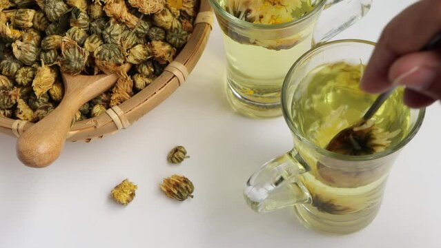 Stir the chrysanthemum tea in the glass with a spoon. Chrysanthemum flower tea and 
dried chrysanthemum buds on white background. healthy beverage concept.