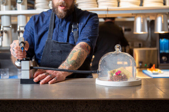 Unrecognizable chef serving tartare with smoking dome