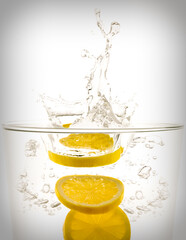 Fototapeta na wymiar Lemon slices splashing into glass of clear liquid