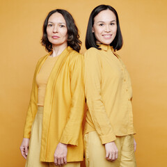 Portrait of serious and smiling multi-ethnic women in yellow clothes standing back to back, womens generation concept