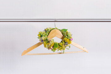 A wreath of flowers hung on a wooden hanger on a white background. Spring, wedding preparations, flowers to decorate the bride's hair. Horizontal photo. - Powered by Adobe