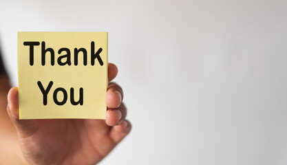 Selective Focus Hand holding yellow sticky note with Thank You word over white background with copyspace.