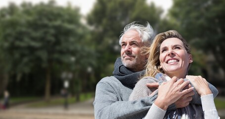 Fototapeta premium Smiling caucasian senior man embracing senior woman against trees in park during sunny day
