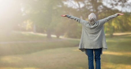 Rear view of caucasian senior woman with arms outstretched standing in park during foggy weather