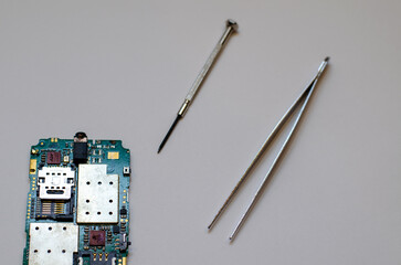 Disassembled mobile phone on the table of a mechanical engineer during repair. Tweezers and screwdriver for repairing electronic gadgets on a white background.