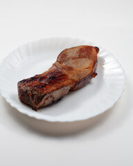 On the table in a plate is a piece of fried meat. On a white background.