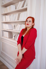 Business woman standing in her office at book-case. Office worker in red suit in her gorgeous cabinet. Company director business portrait