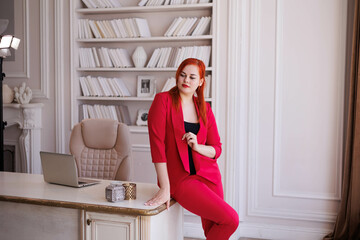 Business woman sitting on her table. Office worker in red suit in her gorgeous cabinet. Company director business portrait