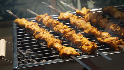 Shashlik - traditional Georgian barbecue. Closeup of raw roasted marinated meat barbecue shish kebab shashlik on steel metal skewers lying grill fire brazier with charcoal.  Making barbecue