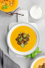 Seasonal autumn roasted pumpkin and carrot soup with cream and rye bread croutons on a light concrete background. Top view.