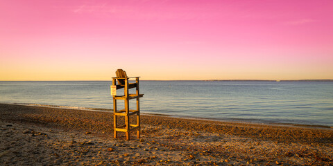Pink sky at sunset at the beach with a lifeguard chair over the sandy shore