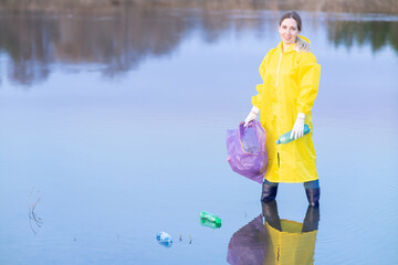 a smiling young woman in rubber boots and bright yellow clothes stands in the river and collects...