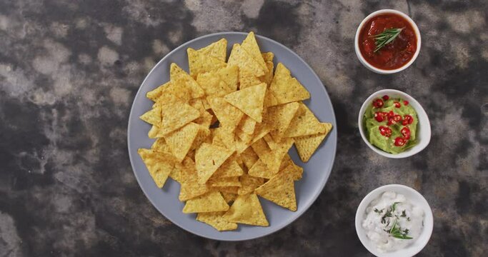 Close up of nachos in a plate and sauces on black surface