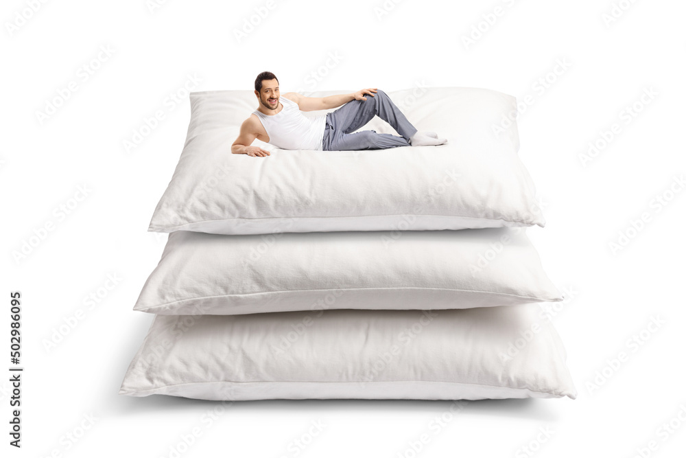 Wall mural young man in pajamas laying on a pile of big pillows