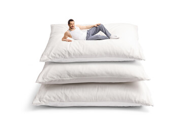 Young man in pajamas laying on a pile of big pillows
