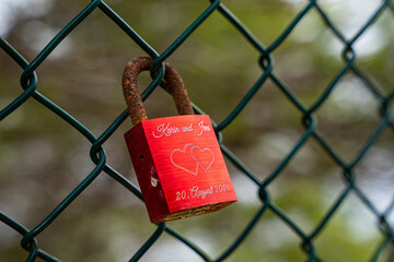 Stara zardzewiała czerwona kłódka wisząca na ogrodzeniu.  Symbol niekończącej się miłości. 