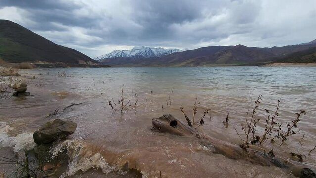 Panning view of muddy water waves lapping on shore of Deer Creek Reservoir in Utah during Spring storm.