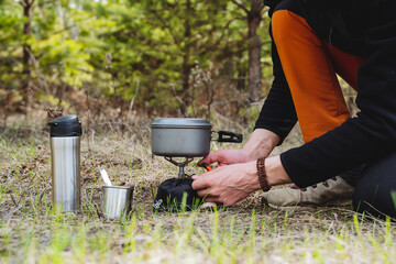 Equipment for a hike, metal utensils for eating, a tourist prepares breakfast in nature, set fire to a gas burner, boil water, a mug, a thermos with tea.