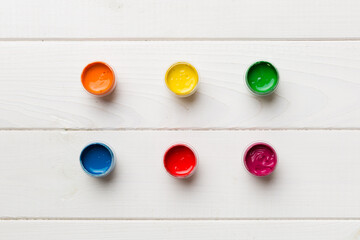 jars with gouache of different colors on Colored background. hobby painting. Top view with empty...